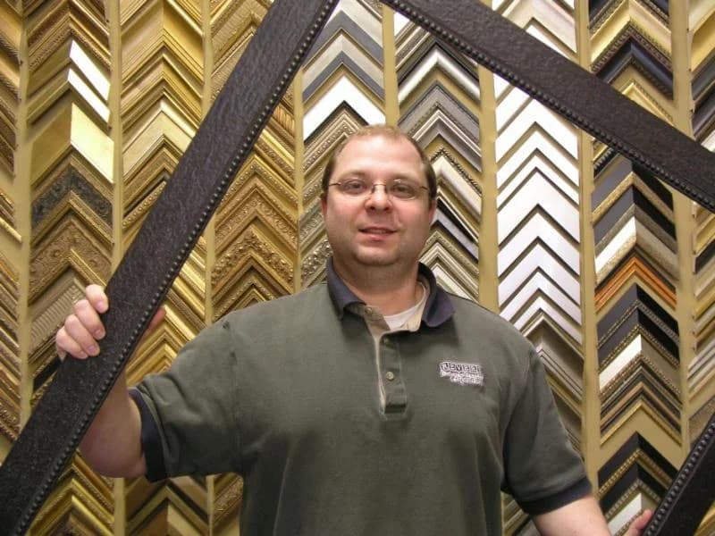 George Kormos holding a large frame in front of Revere's moulding wall.