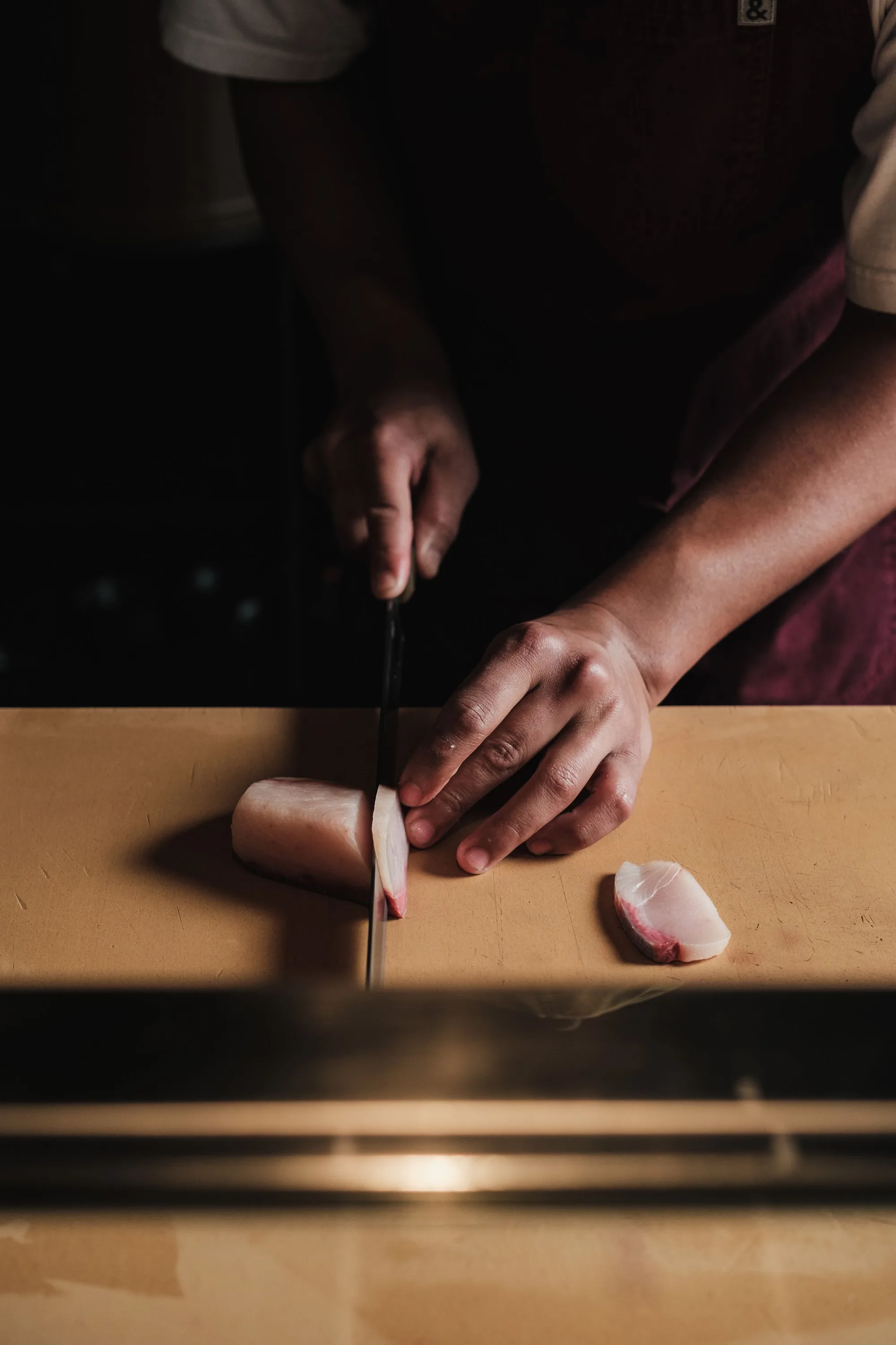 A chef's hands slicing seasonal fish at the counter.