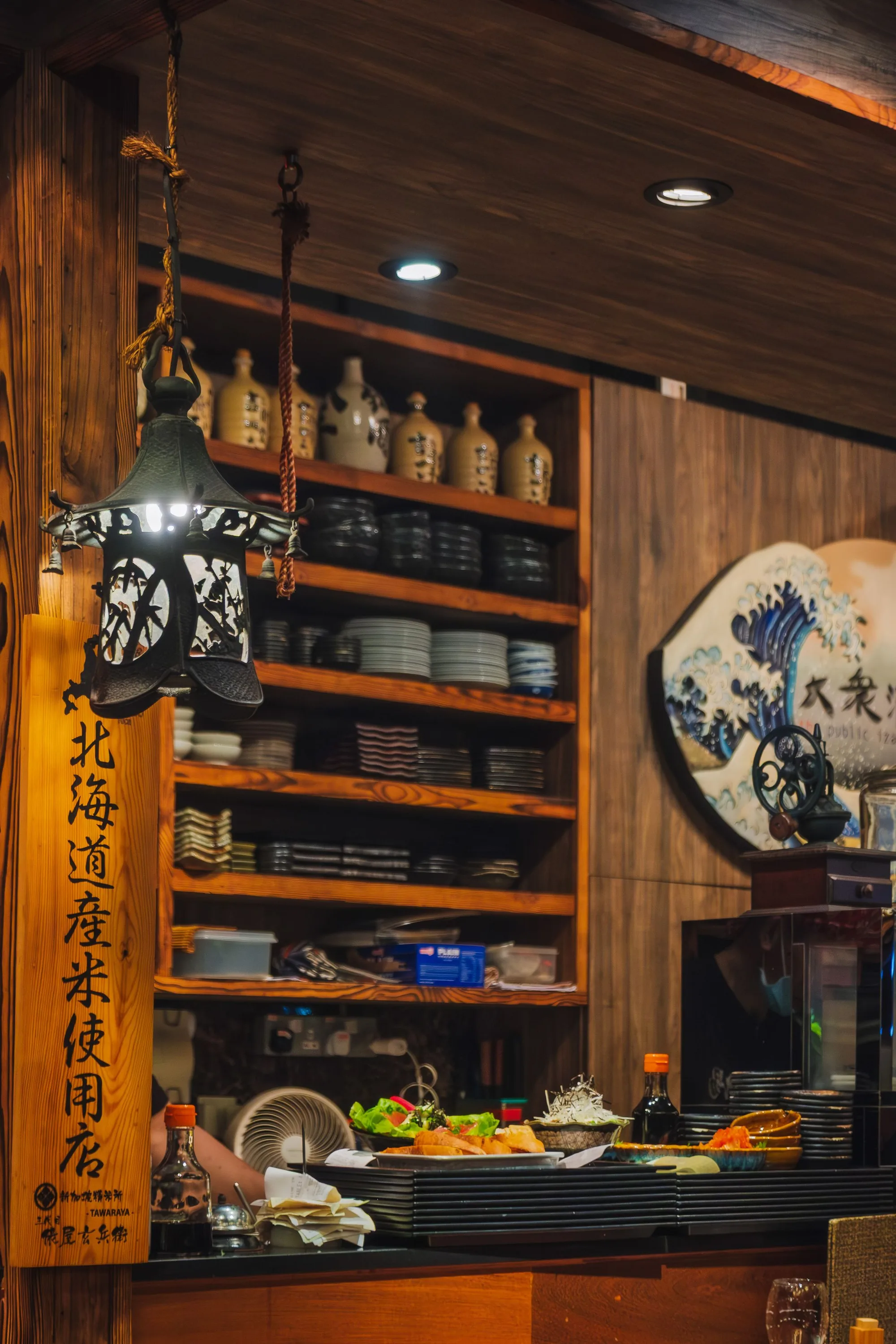 A warmly lit Japanese sushi counter with wood shelving and ceramics.