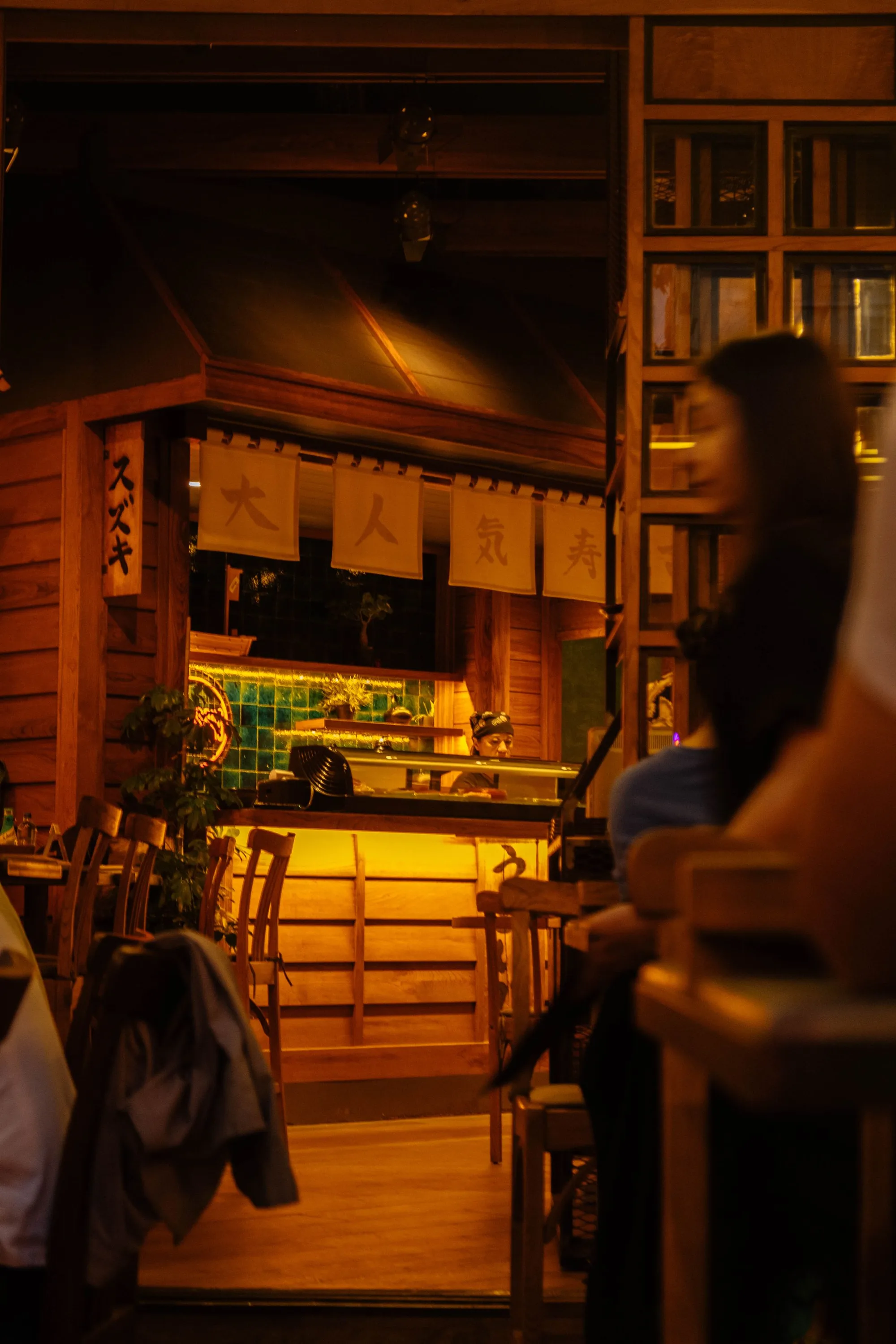 Guests gathered around a warmly lit Japanese counter at night.