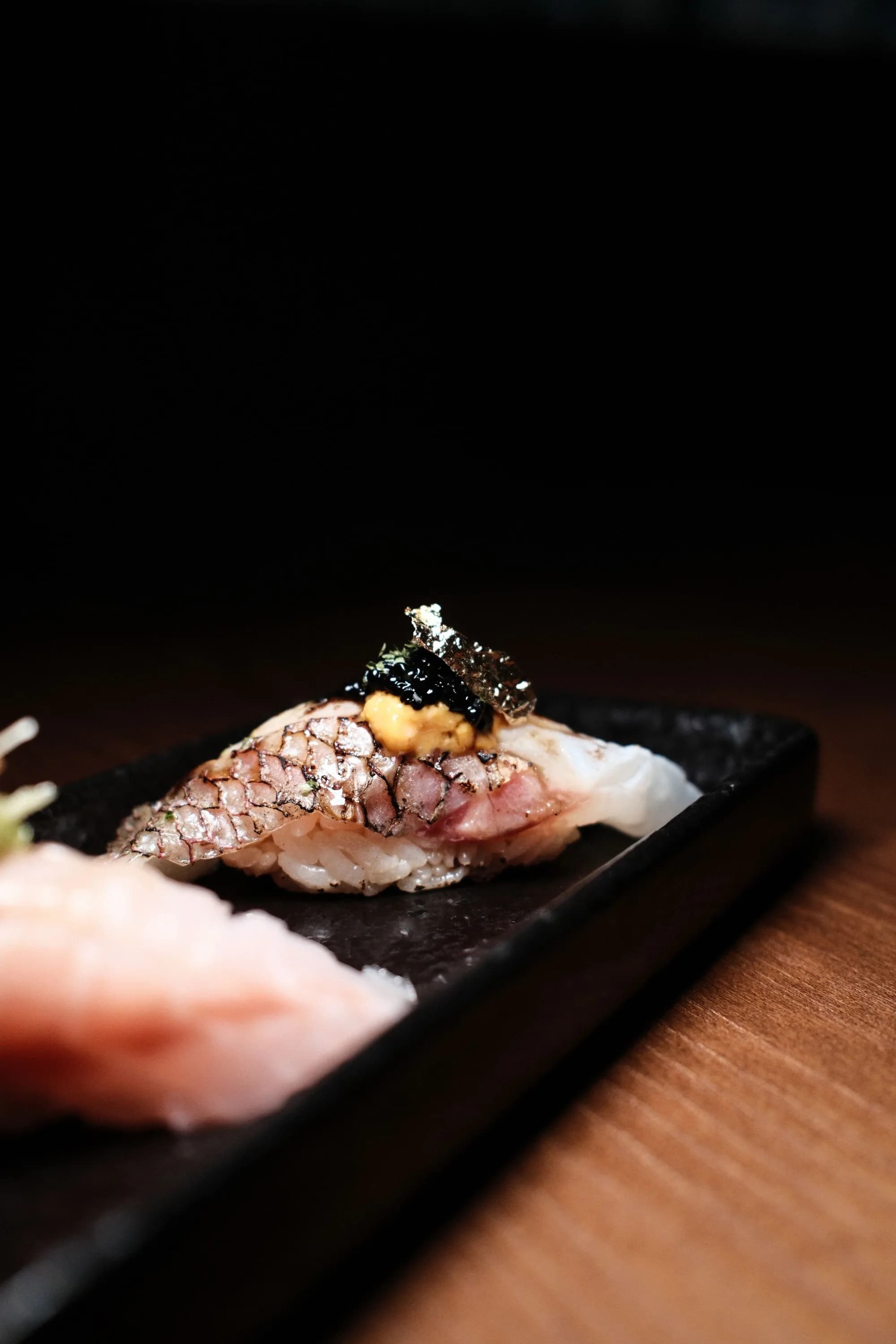 Seared nigiri finished with uni and caviar on a black plate.