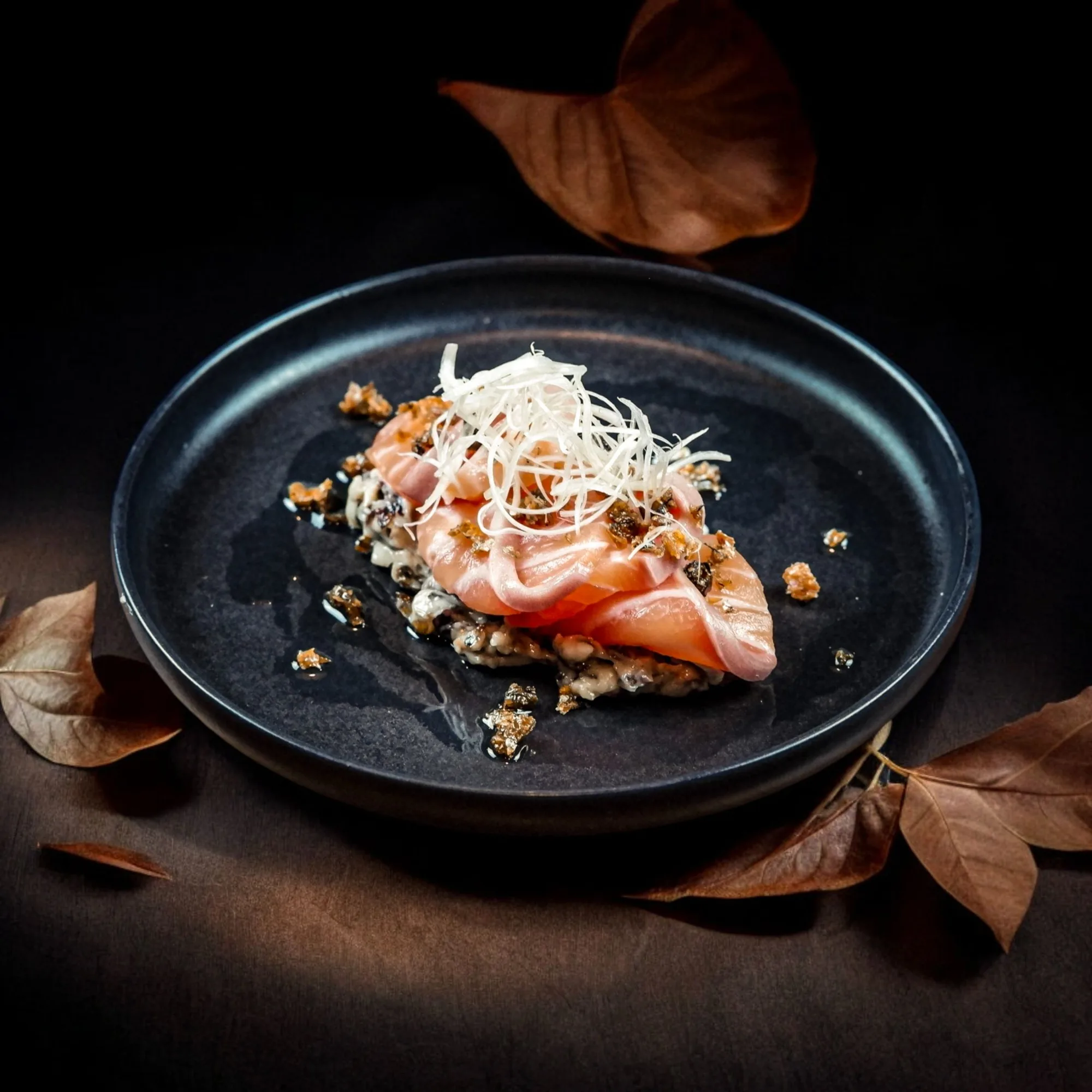 Salmon sashimi arranged with delicate seasonal garnishes on a dark plate.
